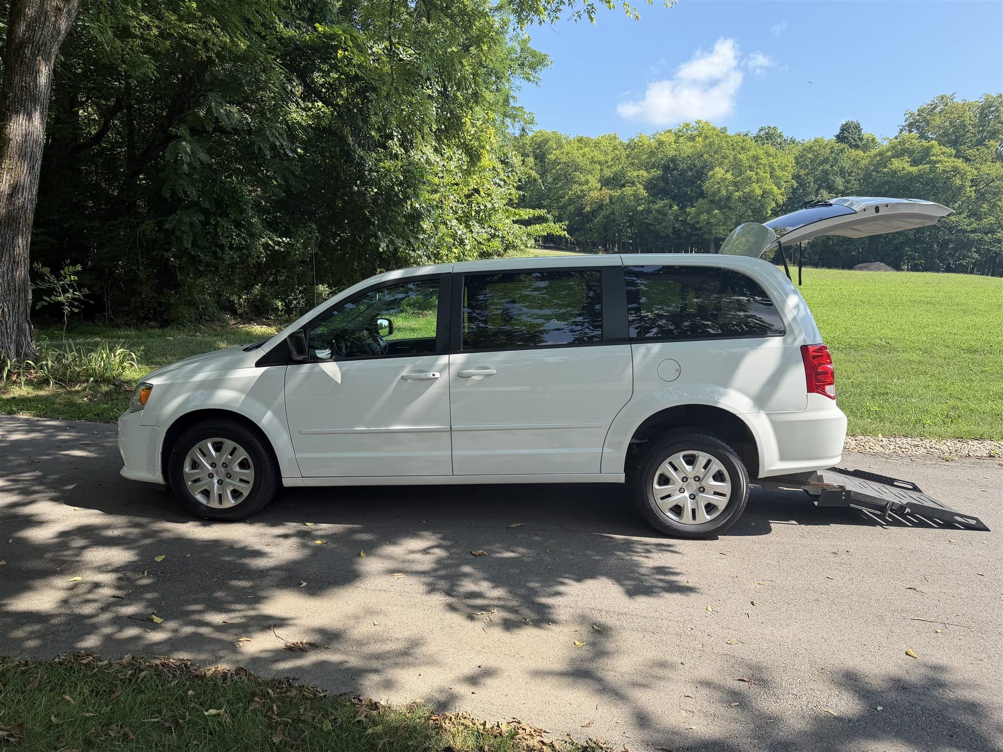 White 2017 Dodge Grand Caravan parked on a shaded drive with its rear wheelchair ramp deployed